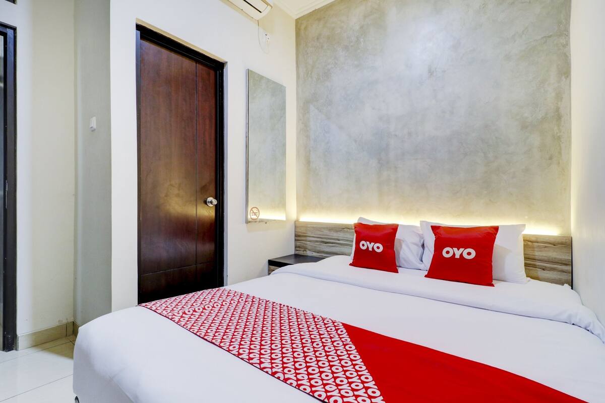 A hotel room with a large bed, a wooden door, and a textured wall behind the bed.