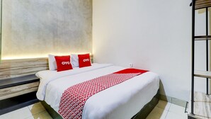 A hotel room with a bed, white bedding, red pillows, a patterned throw, and a wooden headboard. - Hotel O Ada Residence (Karawang)