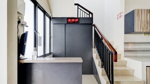 A modern staircase with a digital clock displaying the time, a hand sanitizer dispenser, and a wooden panel on the wall. - Hotel O Ada Residence (Karawang)