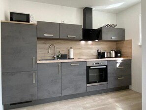 A modern kitchen with grey cabinets, a wooden countertop, a stainless steel sink, and a built-in oven.