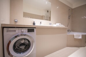 A modern bathroom with a washing machine, a sink, a mirror, and a shower.