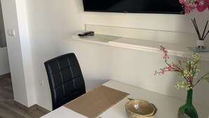 A modern living room with a flat-screen TV mounted on the wall, a black leather chair, a white table with a placemat, a decorative bowl, and a green vase with flowers. - Apartment for 2 in Nerja center (Nerja)