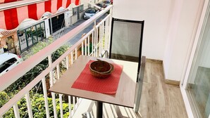 A balcony with a table, a chair, and a view of a street with parked cars and buildings. - Apartment for 2 in Nerja center (Nerja)