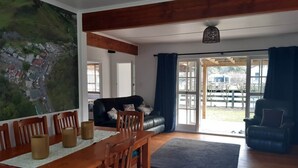 A spacious living room with a wooden dining table, chairs, a black sofa, and a large window with curtains.