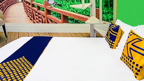Un lit recouvert d’une couvre-lit aux motifs bleus et jaunes, deux oreillers aux motifs similaires, et une vue sur un pont en bois et la verdure, visible à travers une fenêtre.