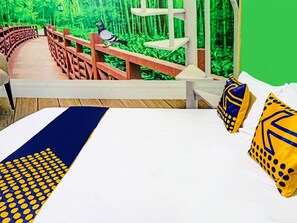 Een bed met een deken met blauw en geel patroon, twee kussens met vergelijkbare designs, en uitzicht op een houten brug en begroeiing door een raam.