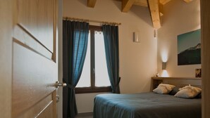 A bedroom with a bed, curtains, a nightstand, and a wall-mounted lamp. - PAESEMIO.CERVAREZZA (Ventasso)
