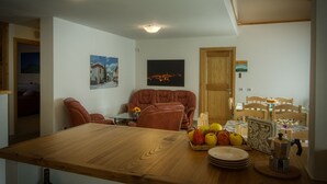 A dining area with a wooden table, chairs, and a fruit basket. There are two paintings on the wall and a wooden door. - PAESEMIO.CERVAREZZA (Ventasso)
