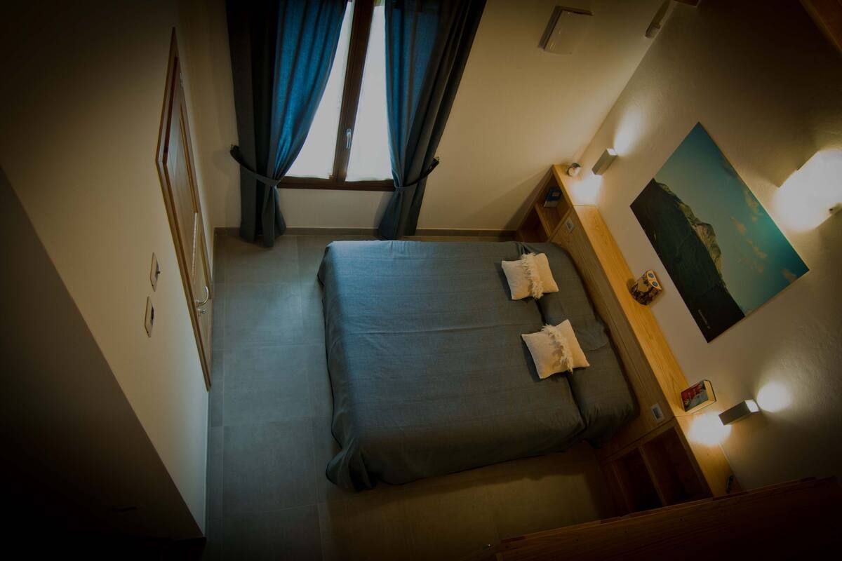 A room with a bed, a nightstand, a wall-mounted shelf, and a painting.