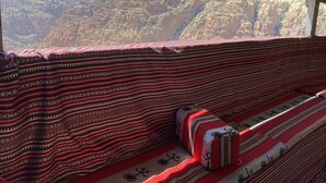 Una habitación con una manta roja y blanca estampada, un cojín y vistas a un paisaje montañoso.