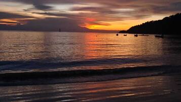 A sunset over a calm sea with boats and a distant shoreline.