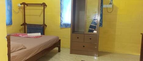 A room with yellow walls, a wooden bed with a headboard, a wardrobe with a mirror, and a small table with a chair.