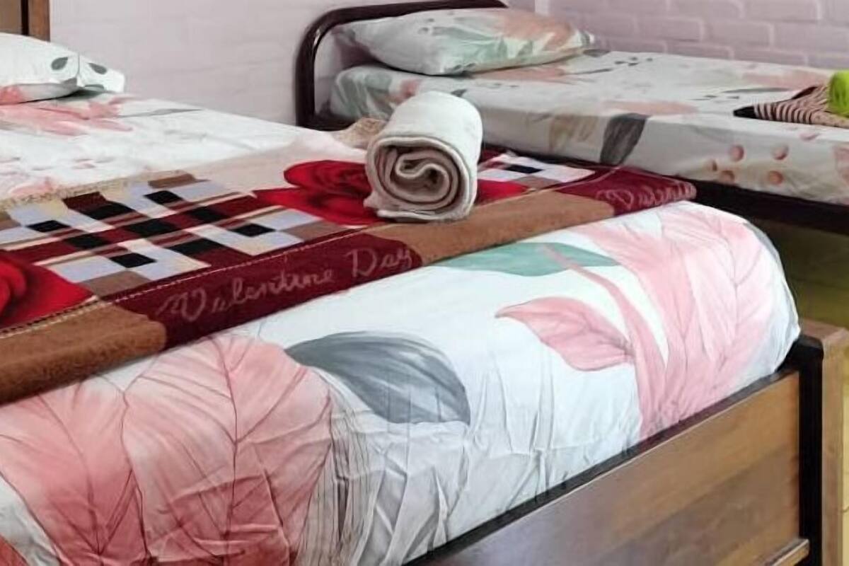Ein ordentlich bezogenes Bett mit floralem Überwurf, einem aufgerollten Handtuch und einem Buch mit dem Titel „Valentinstag“.