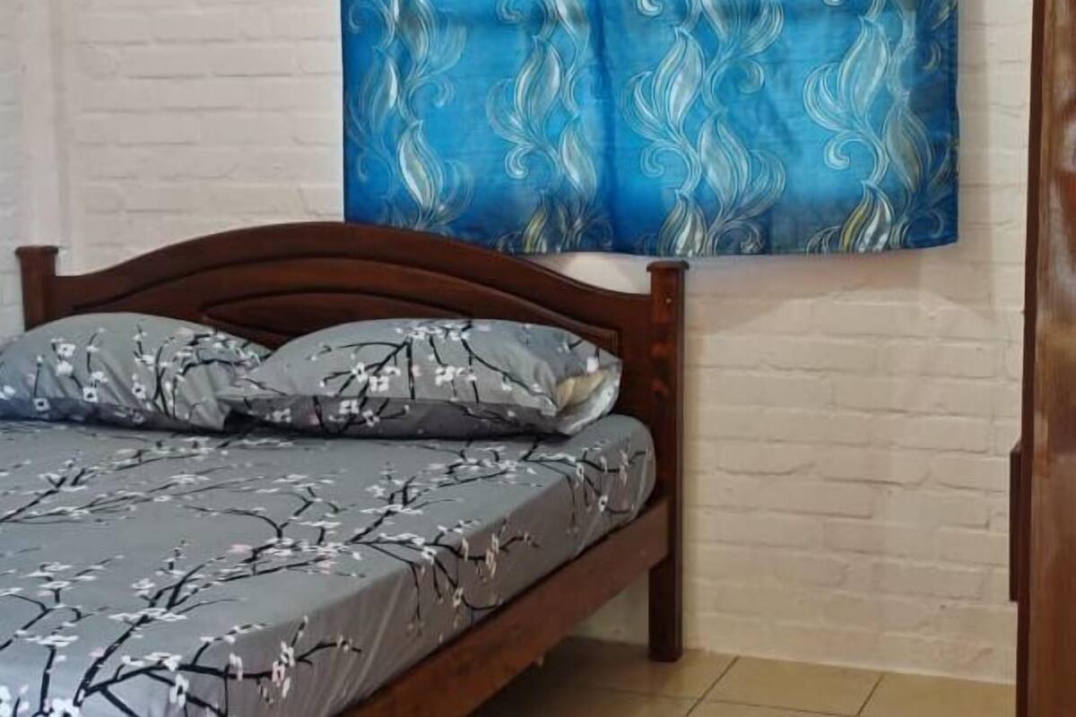 Ein Schlafzimmer mit einem Bett, einem blauen Vorhang mit Blätermotiv und einer weißen Ziegelwand.