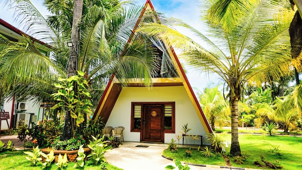 A triangular-shaped building with a wooden door, surrounded by lush greenery and palm trees. - Reecha Kurinji Resort (Iyakachchi)