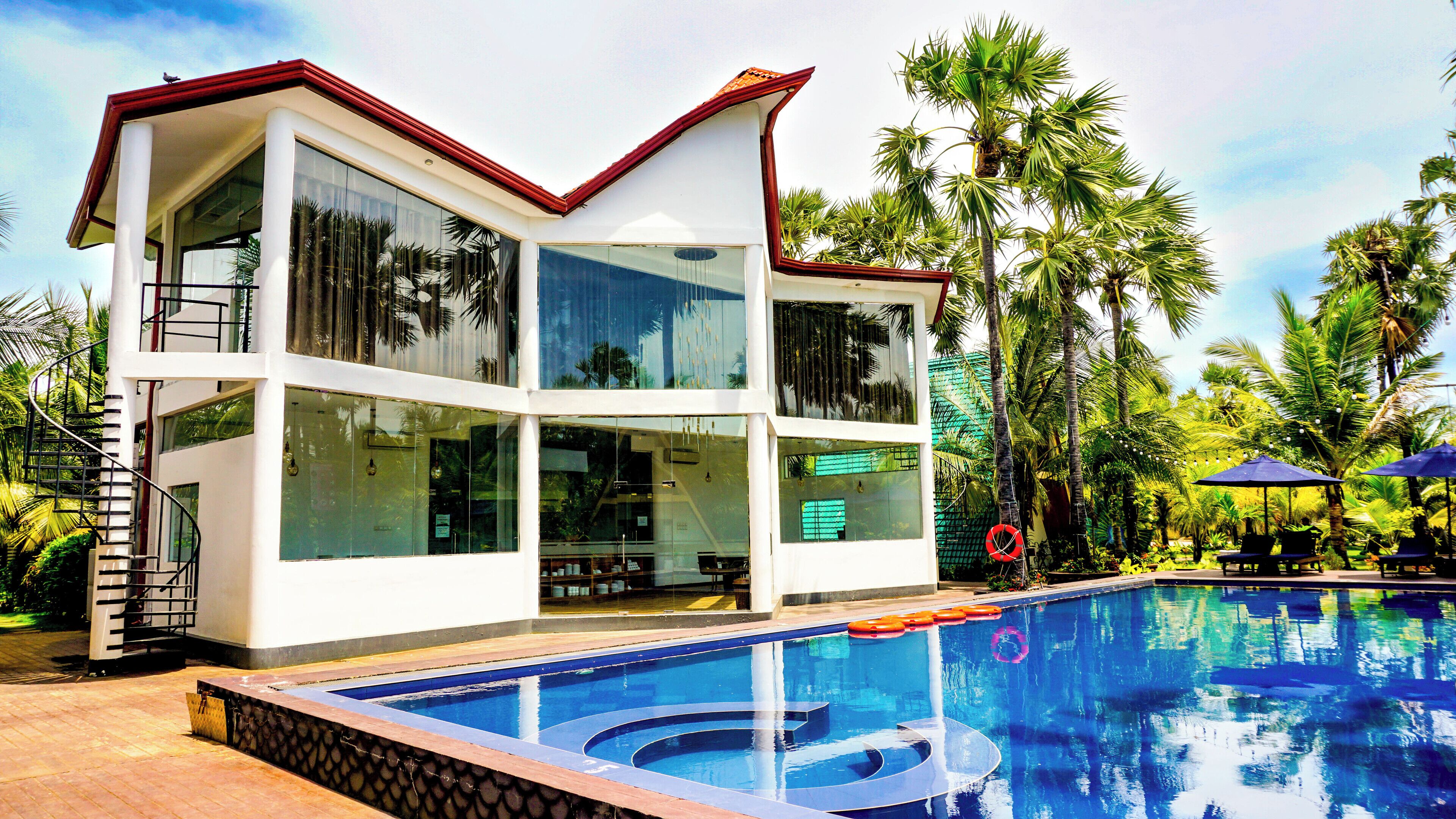 Un bâtiment moderne à deux étages, doté d’une piscine et entouré de palmiers.