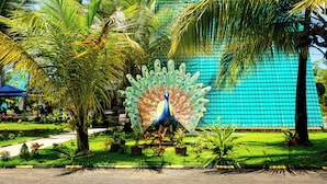 A peacock statue in a garden with palm trees and a blue tiled wall in the background. - Reecha Kurinji Resort (Iyakachchi)
