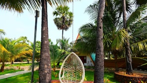 A hanging chair in a tropical garden with palm trees and a stone pathway. - Reecha Kurinji Resort (Iyakachchi)