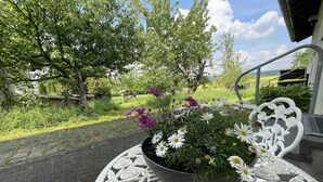 Une vue sur un jardin avec une table et des chaises en métal, le tout entouré de fleurs et d’arbres en pleine floraison.