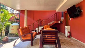 A hotel lobby with a red wall, a staircase, a flat-screen TV mounted on the wall, and two orange chairs. - Villa Noelia Garden Suite - Coatepeque Lake (Lago de Coatepeque)