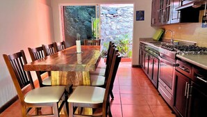 A dining area with a wooden table and chairs, a kitchen with stainless steel appliances, and a view of a stone wall and greenery outside. - Villa Noelia Garden Suite - Coatepeque Lake (Lago de Coatepeque)