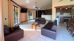 A spacious living area with a sofa, a coffee table, and a television. There is a kitchen area with a refrigerator and stove. - Villa Noelia Paradise Suite - Coatepeque Lake (Lago de Coatepeque)