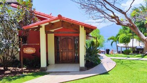 A building with a red roof and a wooden door, surrounded by greenery and a paved walkway. - Villa Noelia Paradise Suite - Coatepeque Lake (Lago de Coatepeque)