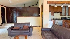 A modern living room with a sofa, a coffee table, and a kitchen area with cabinets and appliances. - Villa Noelia Paradise Suite - Coatepeque Lake (Lago de Coatepeque)