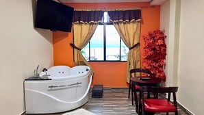 A room with a bathtub, a table with chairs, a television, and a window with curtains. - Villa Noelia Calli Suite - Coatepeque Lake (Lago de Coatepeque)