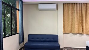 Een kamer met een blauwe bank, een airconditioning, een vloer met patroon, en een raam met uitzicht op bomen.