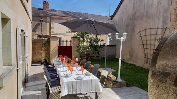 An outdoor dining area with a table set for four, surrounded by chairs, under a large umbrella. - Maison Anjou 13 Personnes (Montreuil-Bellay)