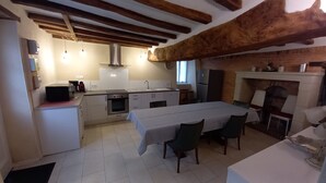 A compact kitchen with a dining area, featuring exposed wooden beams, a built-in oven, and a fireplace. - Maison Anjou 13 Personnes (Montreuil-Bellay)