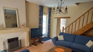 A living room with a fireplace, a television, a blue sofa, a wooden coffee table, and a staircase. - Maison Anjou 13 Personnes (Montreuil-Bellay)
