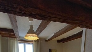 A small, cozy bedroom with a single bed, a nightstand with a lamp, a window with curtains, and a wooden ceiling. - Maison Anjou 13 Personnes (Montreuil-Bellay)