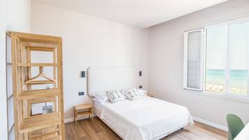 Ein Schlafzimmer mit einem Bett, einer Holztruhe, einem Nachttisch, einem Stuhl und einem Fenster mit Blick auf den Strand.