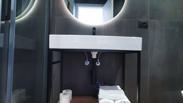 Un baño moderno con un espejo redondo, un lavamanos blanco y un estante con toallas y papel higiénico.