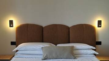 Una cama bien hecha con sábanas blancas y una sola almohada, flanqueada por dos lámparas fijadas a la pared.