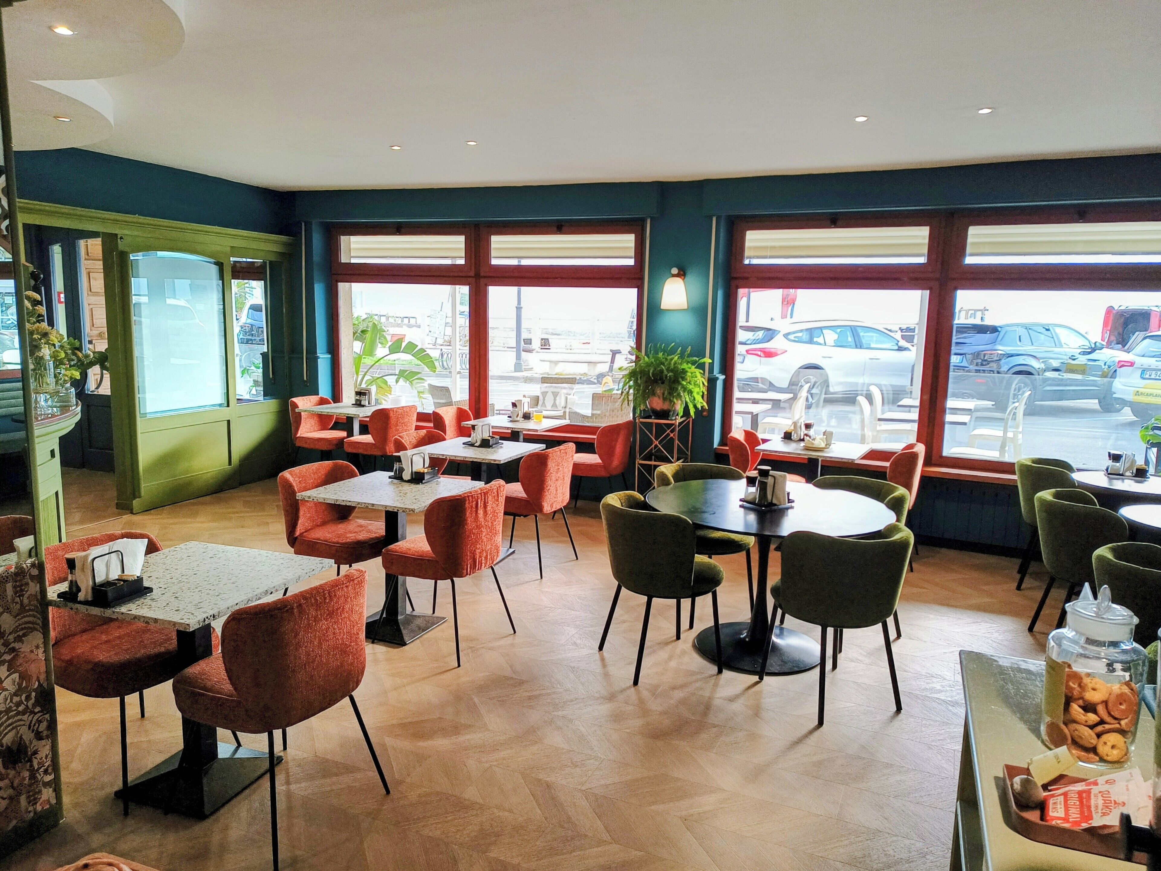A restaurant with tables and chairs, large windows, and a view of the street.