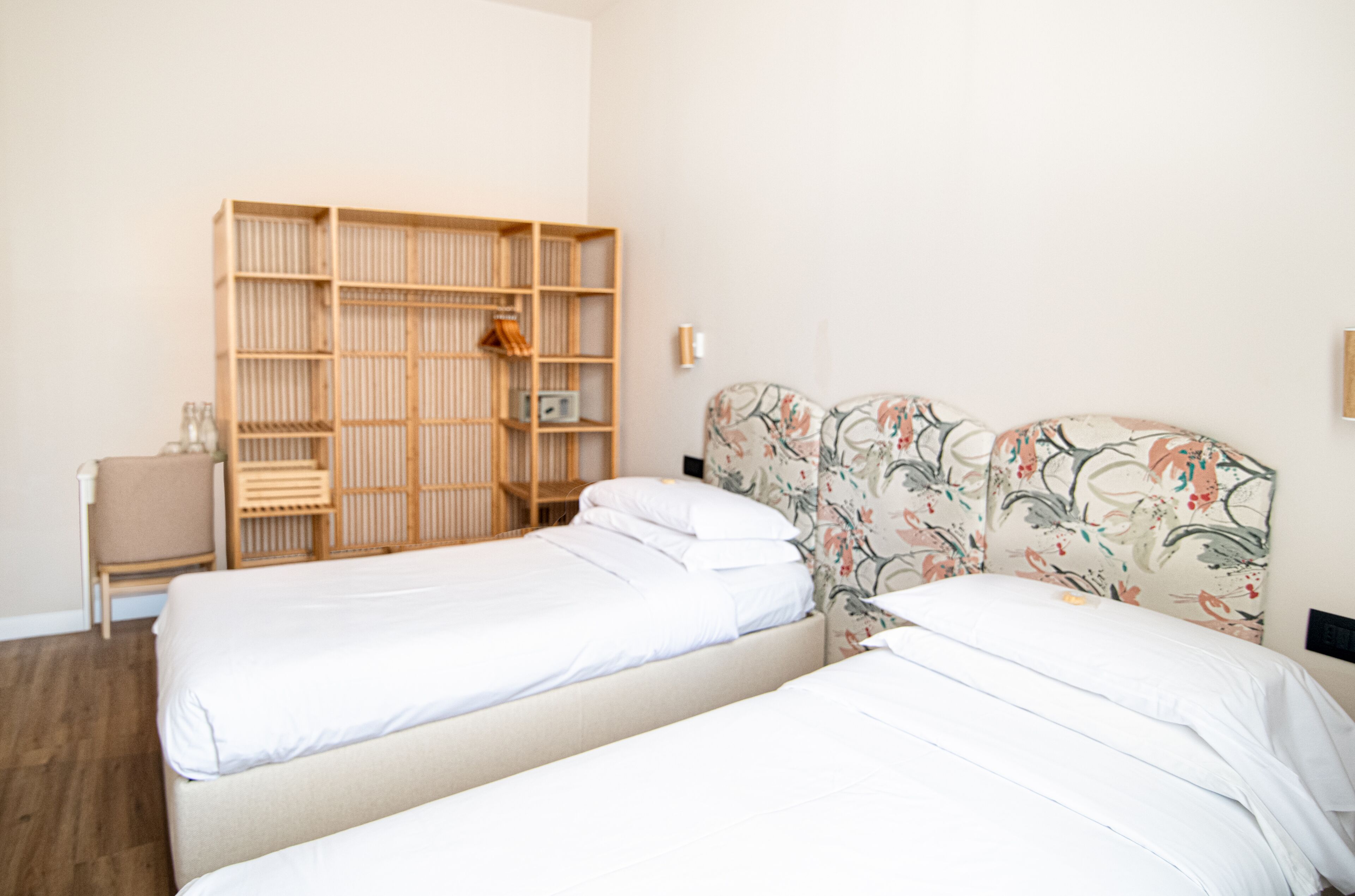 A room with two beds, a wooden wardrobe, a small table, and a floral headboard.