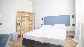 A modern hotel room with a large bed, a wooden wardrobe, a small seating area, and a bedside table.