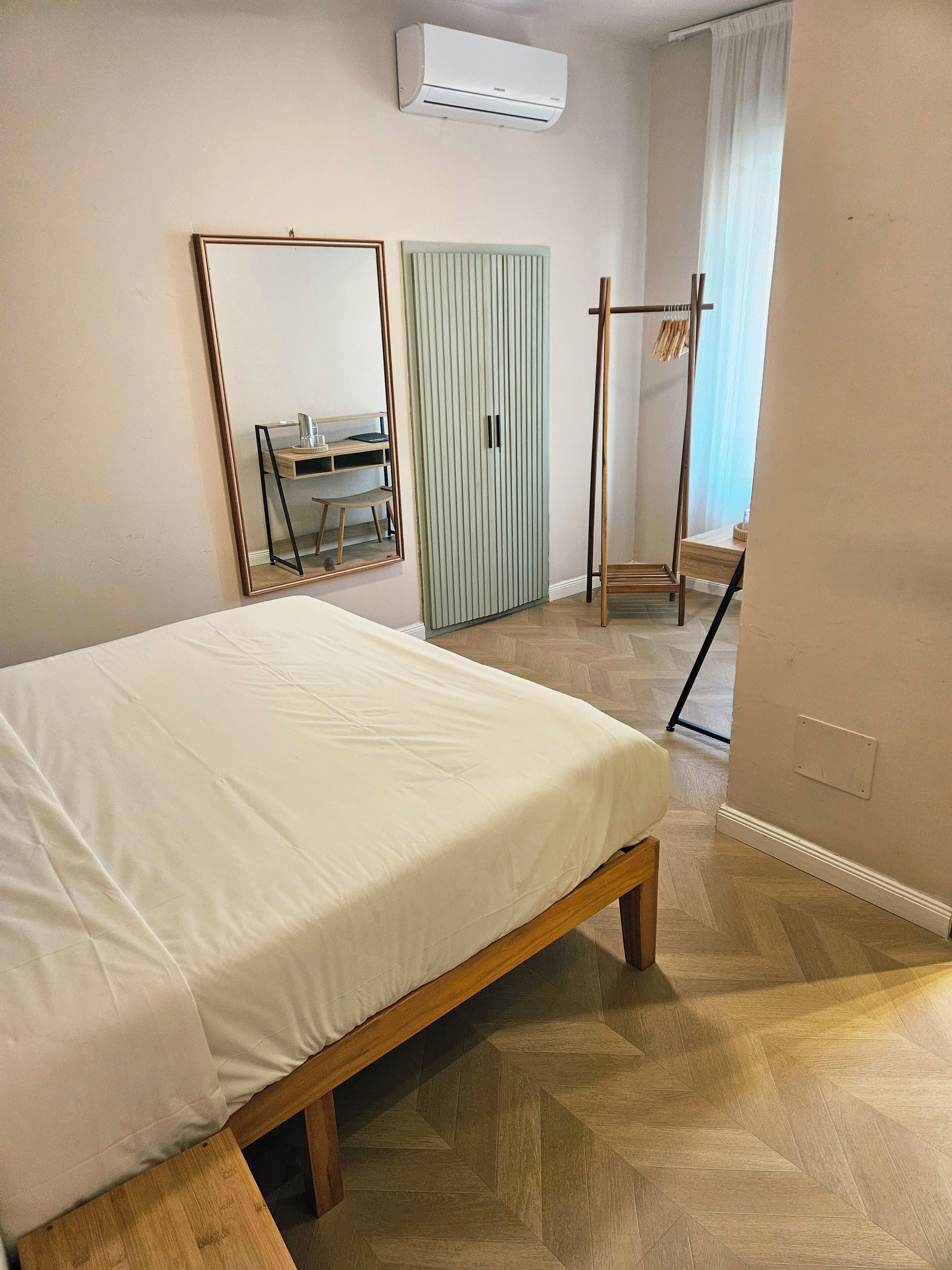 Une chambre à coucher comprenant un lit, une armoire, un miroir, un bureau et un appareil de climatisation.