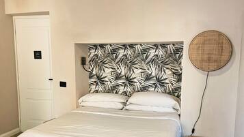 Une chambre à coucher avec un lit, une petite table de chevet en bois, une lampe ronde fixée au mur et une porte avec une pancarte.