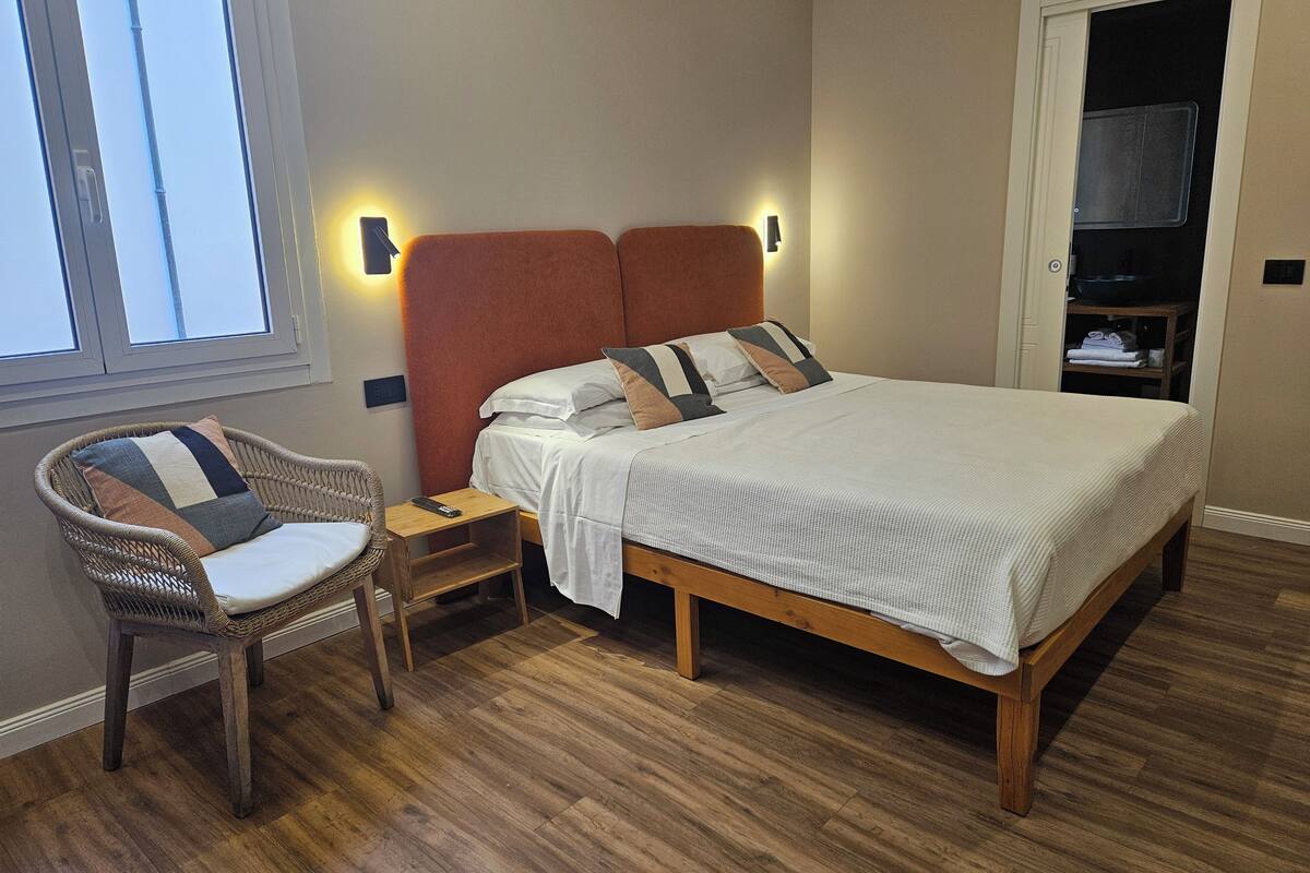 Une chambre à coucher avec un lit en bois, une table de chevet, une chaise en osier et une armoire.