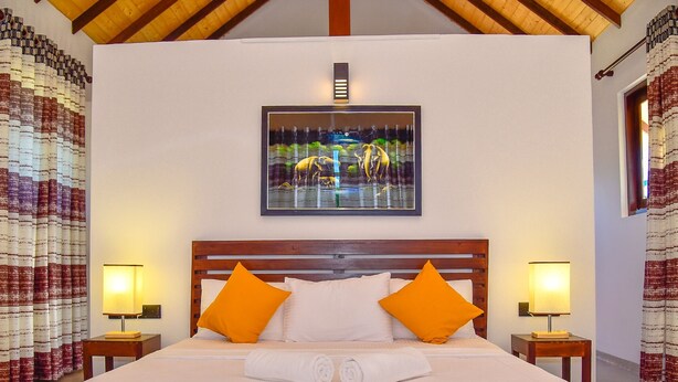 Une chambre d’hôtel avec une tête de lit en bois, deux oreillers orange, une couvre-lit blanche et un tableau au-dessus du lit.