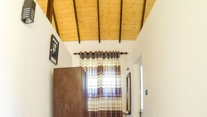 Un couloir étroit avec un plafond en bois, une porte sur la droite et un rideau à rayures au fond.