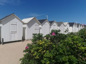 A row of white beach huts with a sandy ground in front.