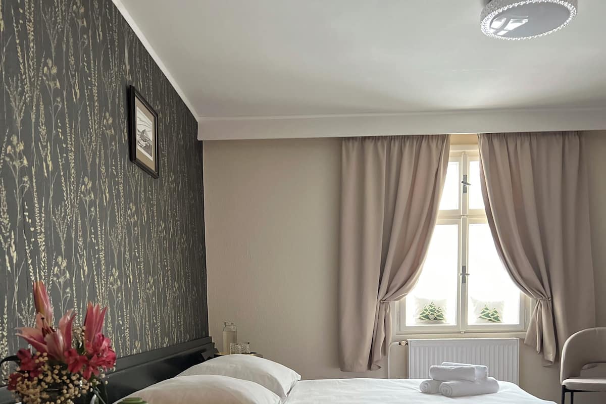 A hotel room with a bed, a nightstand, a chair, and a window with curtains.