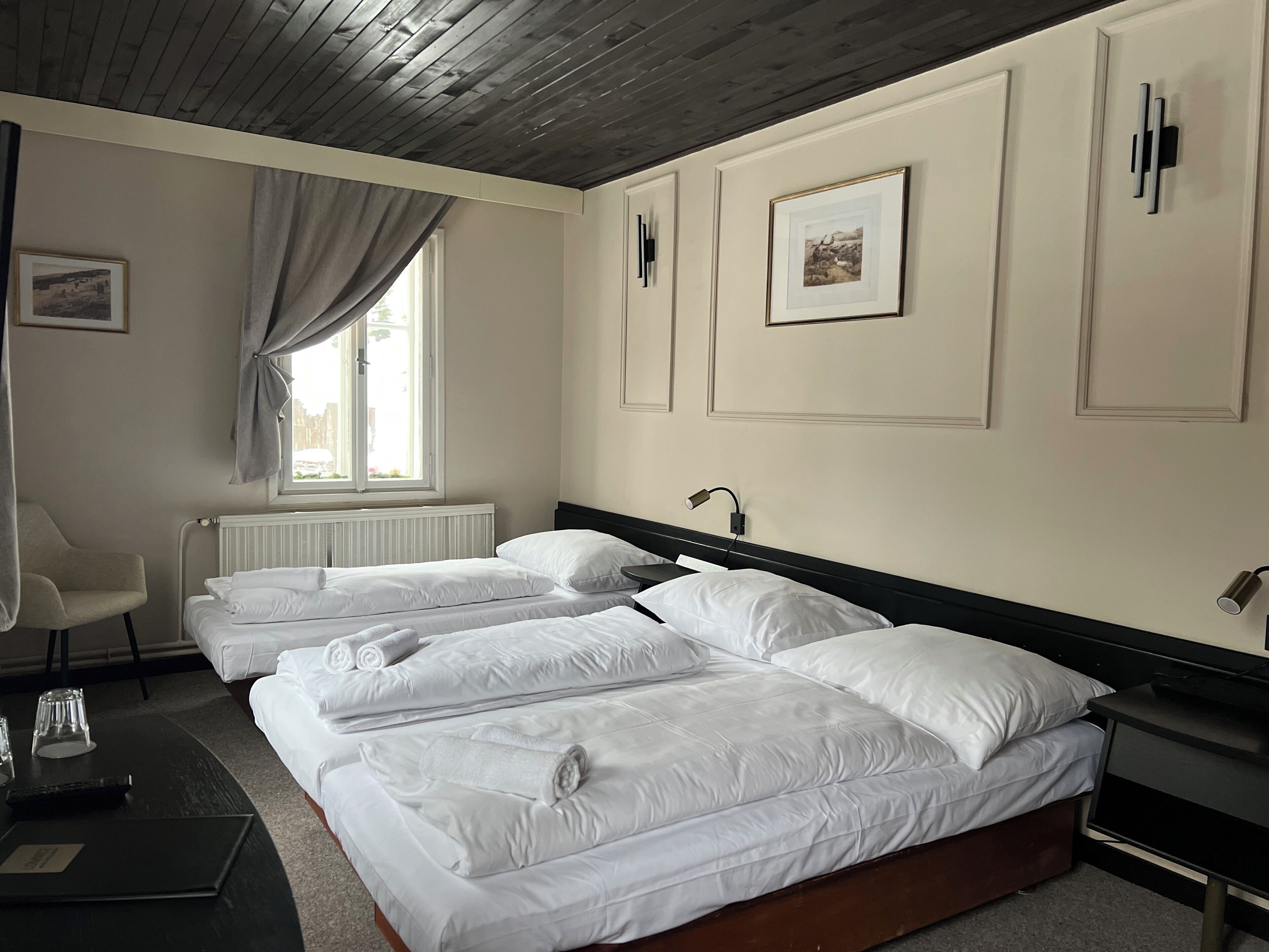 A hotel room with two beds, a chair, a desk, and a window with curtains.