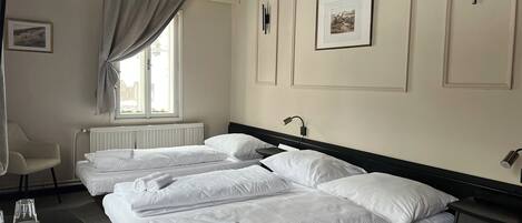 A hotel room with two beds, a chair, a desk, and a window with curtains.