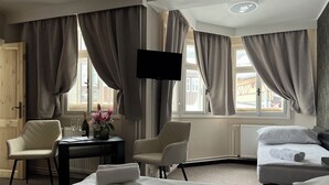 Habitación de hotel con dos camas, un escritorio con silla, televisor montado en la pared y ventanas amplias con cortinas.